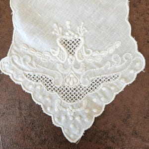 Peut inclure: Un mouchoir blanc vintage avec des motifs floraux et géométriques brodés. Les bords sont festonnés et le motif comprend des détails ajourés. Le mouchoir est fait d'un tissu fin et délicat.