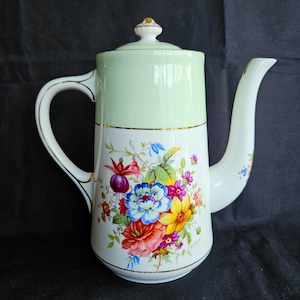 May include: A vintage porcelain coffee pot. The top is light green, the base white, decorated with a colourful floral pattern. The handle and spout are white, with gold trim. The lid has a gold finial. A classic piece for serving.
