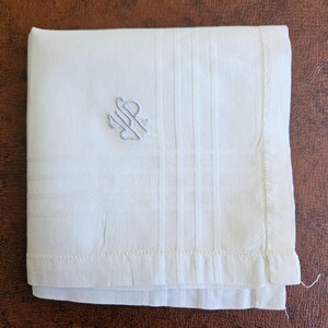May include: Ivory-colored handkerchief with a subtle striped pattern and a delicate embroidered monogram in the upper left corner. The edges are neatly hemmed. This classic accessory is perfect for formal occasions.