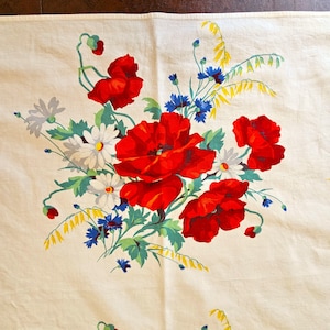 May include: Cream-colored tablecloth featuring a vibrant floral design. The pattern includes large red poppies, white daisies, blue cornflowers, and yellow accents. Green leaves and stems complete the botanical arrangement, creating a cheerful and colorful aesthetic.