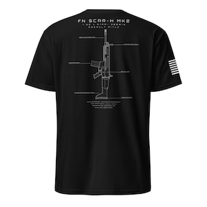 Może przedstawiać: Czarna koszulka z białym schematem karabinu szturmowego FN SCAR-H MK2. Koszulka zawiera specyfikacje karabinu i mały amerykański wzór flagi na rękawie.