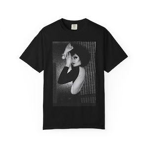 May include: Black t-shirt featuring a black and white image of a person with dark hair and makeup. The text "SIOUXSIE AND THE BANSHEES" is printed vertically on the left side of the image. The shirt has a classic crew neck and short sleeves.