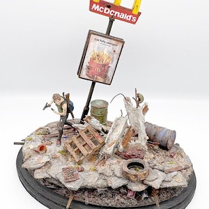 May include: A detailed diorama featuring a post-apocalyptic scene with a McDonald's sign. The sign displays the golden arches and the text "McDonald's". A figure with a gun is running through the debris. The sign below says "Get fully charged".