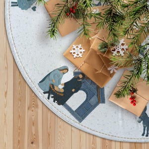 May include: A light-colored Christmas tree skirt with a nativity scene and a donkey illustration. The skirt is decorated with brown wrapped gifts, snowflakes, and evergreen branches with red berries.
