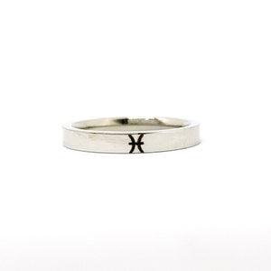 May include: A silver band ring with a Pisces zodiac symbol engraved on the top.