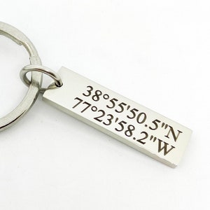 May include: Silver keychain with a rectangular tag engraved with the coordinates 38°55'50.5"N 77°23'58.2"W.