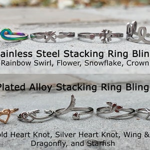 May include: A collection of stacking rings in silver and rose gold featuring various designs, including a heart knot, a flower, a snowflake, a crown, a dragonfly, a wing and heart, and a starfish.  The text "Stainless Steel Stacking Ring Bling: Rainbow Swirl, Flower, Snowflake, Crown" and "Plated Alloy Stacking Ring Bling: Rose Gold Heart Knot, Silver Heart Knot, Wing & Heart, Dragonfly, and Starfish" is displayed below the rings.
