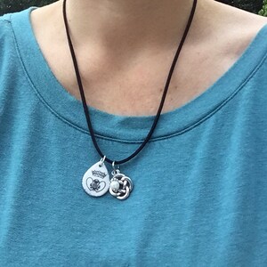 May include: A black cord necklace with two silver pendants. One pendant is a teardrop shape with a white design and the other is a Celtic knot.