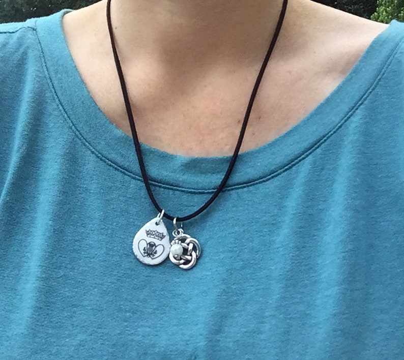 May include: A black cord necklace with two silver pendants. One pendant is a teardrop shape with a white design and the other is a Celtic knot.