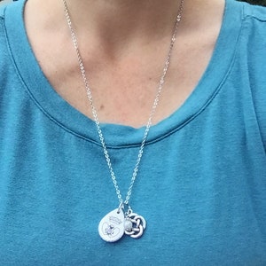 May include: A silver chain necklace with a silver pendant featuring a small bee and the words "Wonder Woman" and a silver Celtic knot charm.