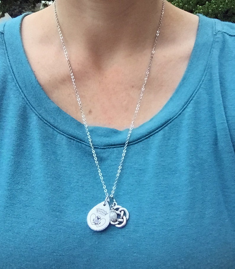 May include: A silver chain necklace with a silver pendant featuring a small bee and the words "Wonder Woman" and a silver Celtic knot charm.