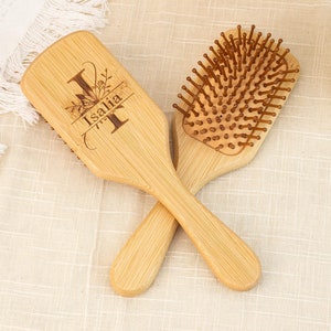 Puede incluir: Dos cepillos para el cabello de madera, uno con una inscripción personalizada que dice "Isalia" y un diseño floral, y el otro con un cepillo de cerdas marrones.
