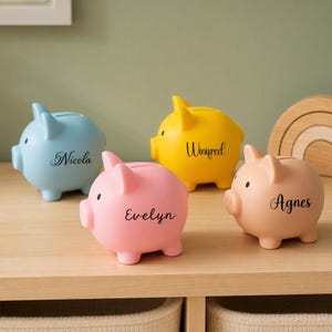 Può includere: Quattro salvadanai in ceramica a forma di maialino nei colori azzurro, giallo, rosa e pesca. Ogni salvadanaio presenta un nome scritto in nero sul lato: Nicola su quello azzurro, Winifred su quello giallo, Evelyn su quello rosa e Agnes su quello pesca.