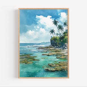 May include: A watercolour painting of a tropical coastal scene. The artwork depicts a turquoise ocean, rocky shoreline, and palm trees under a bright blue sky with white clouds. The painting is framed in a light wood frame.