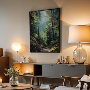 May include: A living room scene featuring a framed forest landscape painting, a table lamp with a glass base, and a modern gray cabinet. A round table holds a vase with greenery and a lit candle. The room is bathed in warm light.