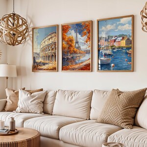 May include: Three framed watercolor prints depicting European landmarks. The first shows the Colosseum, the second the Eiffel Tower, and the third a harbor scene with boats. The prints are in wooden frames and hang above a cream-colored sofa.