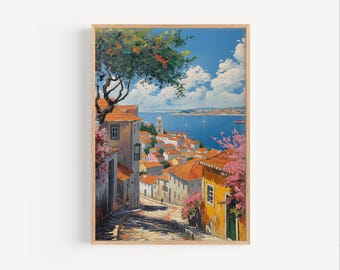 Può includere: Una stampa artistica incorniciata di una città costiera europea. Il dipinto raffigura una strada acciottolata che conduce a un lungomare con edifici con tetti di tegole arancioni. Il cielo è blu con soffici nuvole bianche e la scena è incorniciata da un bordo di legno.