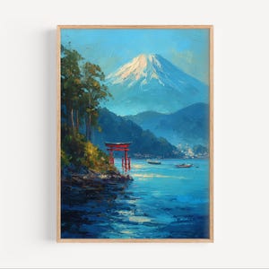 May include: Oil painting of a Japanese landscape featuring Mount Fuji with a snow-capped peak. A red torii gate stands on the shore of a blue lake. The artwork is framed in a light brown wooden frame.
