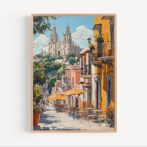 May include: A framed art print showing a sunlit street scene with a cathedral in the distance. Buildings are painted in warm yellow and peach tones, with outdoor seating under yellow parasols. The sky is a bright blue with fluffy white clouds.