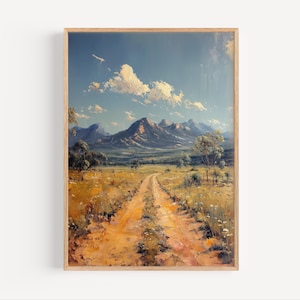 Könnte beinhalten: Gerahmtes Landschaftsgemälde mit einem Feldweg, der durch ein Feld zu fernen Bergen unter blauem Himmel mit Wolken führt. Das Kunstwerk verwendet warme Töne von Gelb, Braun und Grün und schafft eine ruhige, natürliche Szene. Das Gemälde ist in einem Holzrahmen.