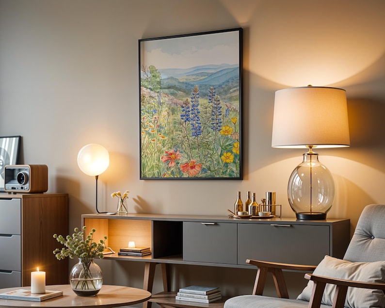 Puede incluir: Una escena de sal&oacute;n con una pintura de acuarela enmarcada de un prado de flores silvestres. Una l&aacute;mpara de cristal con una pantalla blanca y una base de cristal transparente se encuentra sobre un mueble gris. Una mesa redonda tiene una vela y un jarr&oacute;n de vegetaci&oacute;n.