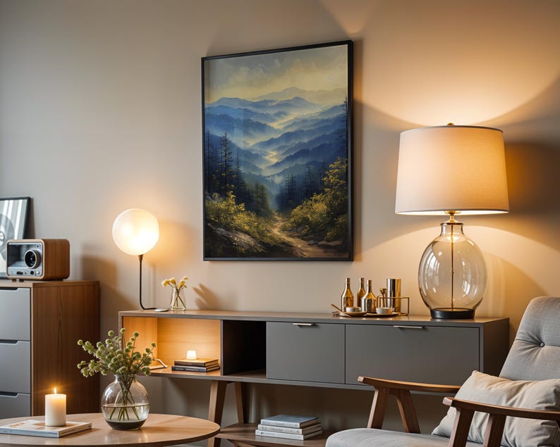 May include: A living room interior with a gray couch, a wooden coffee table, a side table with a lamp, and a framed painting of a mountain landscape. The painting is in a black frame and features a blue and green color scheme.