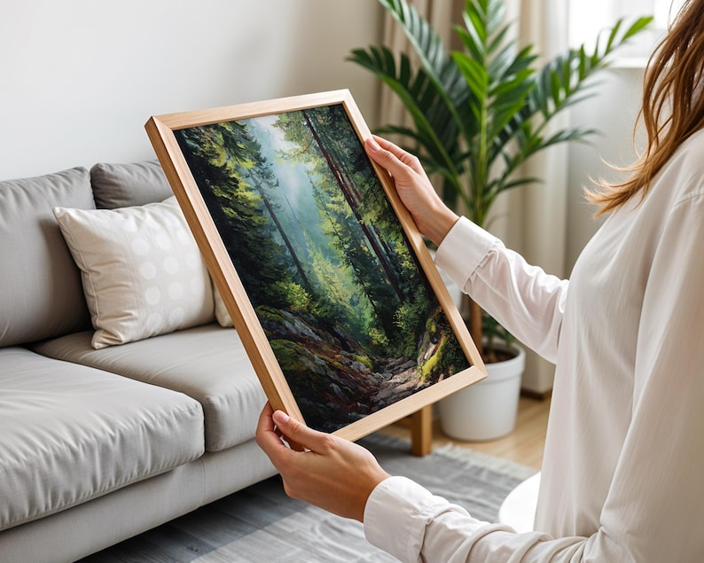 May include: A framed landscape painting depicting a lush forest scene with tall trees and a winding path. The artwork features a palette of greens, browns, and blues, creating a sense of depth and tranquility. The frame is made of light-colored wood.