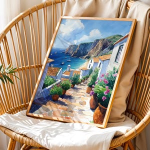 May include: A watercolor painting of a coastal village with white houses, a blue sea, and green hills. The painting is framed in a wooden frame and is sitting on a wicker chair.