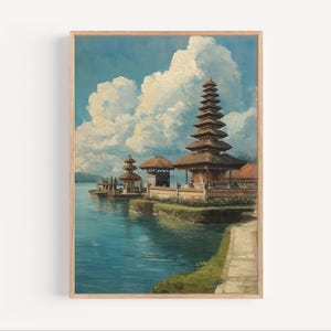 May include: A framed painting depicts a serene waterscape with traditional Balinese temples. The artwork features a multi-tiered pagoda, other structures, and a calm lake under a cloudy blue sky. The painting is in a wooden frame.