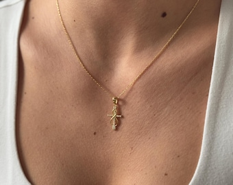 May include: A gold-colored necklace with a pendant in the shape of a cross and an infinity symbol. The pendant is adorned with small, sparkling stones. The necklace is displayed on a person wearing a white shirt.
