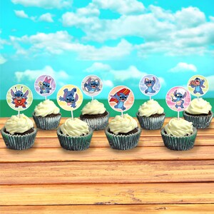 May include: Cupcakes with white frosting and decorative toppers featuring the character Stitch from Lilo & Stitch. The cupcakes sit on a wooden surface against a backdrop of a blue sky with clouds. The toppers have different images of Stitch.