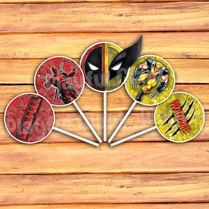 Op de afbeelding: Vijf ronde, kleurrijke taarttoppers met de Marvel-personages Deadpool en Wolverine. De toppers zijn op witte stokjes en hebben een rood, geel en zwart kleurenschema.