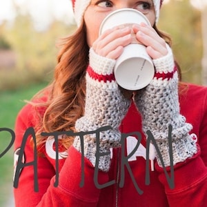 Op de afbeelding: Een paar grijze en witte vingerloze handschoenen met rode en witte strepen aan de manchet. De handschoenen zijn gehaakt en worden gedragen door iemand die een kop koffie vasthoudt.