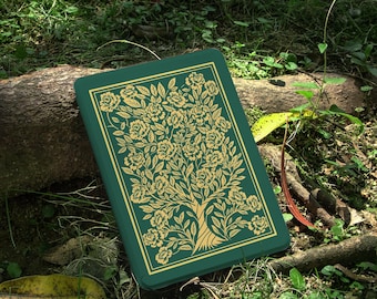 May include: A green journal with a gold floral tree design. The journal is rectangular and has a gold border. The image is set outdoors on a bed of grass and leaves. The text "happylifeenjoydesign" is in the upper right corner.