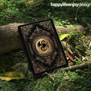 Puede incluir: Funda negra para tableta con un emblema de dragón dorado en un marco circular. La funda tiene un diseño vintage ornamentado con filigranas doradas sobre un fondo negro. El texto "happylifeenjoydesign" está en la esquina superior derecha.