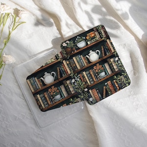May include: A clear phone case with a decorative insert featuring a bookshelf design. The insert showcases a dark green background with wooden shelves filled with books, teapots, and floral accents. The text "happylifeenjoydesign" is visible.