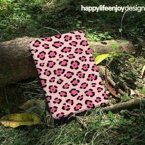 May include: A pink and black leopard print case. The case is rectangular and features a repeating pattern of pink spots with black outlines. The words "happylifeenjoydesign" are in the upper right corner.
