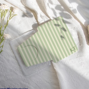 Puede incluir: Una funda transparente para teléfono con un inserto a rayas verdes y blancas. El inserto tiene las iniciales "KT" en la esquina inferior derecha. El texto "happylifeenjoydesign" está en la parte inferior izquierda.