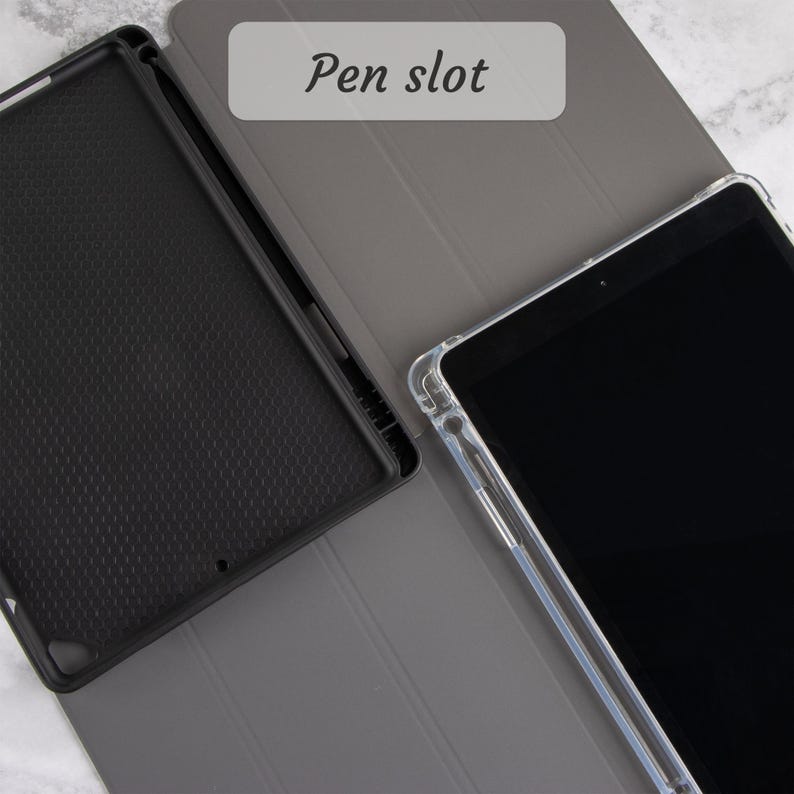 Może przedstawiać: Etui na tablet z czarnym wnętrzem i szarą obudową. Etui jest otwarte, odsłaniając wnętrze i tablet z przezroczystym etui ochronnym. Tekst "Pen slot" jest widoczny na szarej okładce.