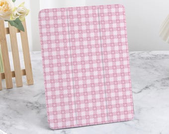 Può includere: Una custodia per tablet con motivo a quadretti rosa e bianco. La custodia è aperta, rivelando l'interno. È realizzata in un materiale liscio e ha una chiusura magnetica. La custodia è progettata per proteggere il tablet da graffi e altri danni.