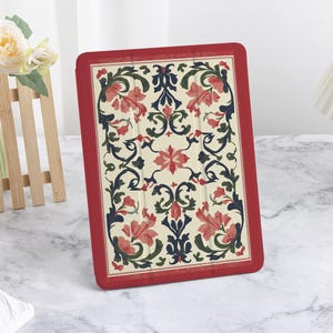 Può includere: Una custodia rossa per tablet con un motivo floreale. La custodia presenta uno sfondo color crema con un motivo di fiori rossi, foglie verdi e accenti blu scuro. La custodia ha un bordo rosso.