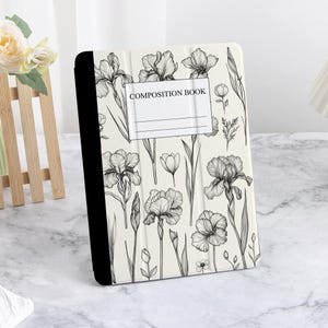 May include: A white composition book with a black and white floral design featuring irises. The cover has the text "COMPOSITION BOOK" printed on it.