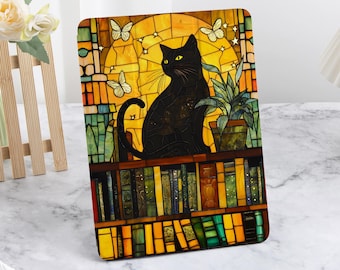 May include: A black cat sits on a shelf filled with books. The cat is looking to the left. The background is a stained glass window with a yellow sun and butterflies.