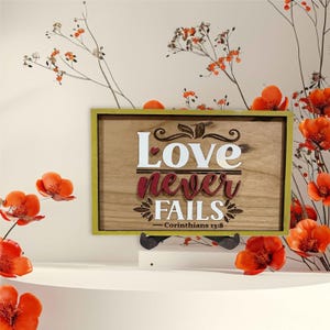 May include: Wooden sign with a yellow frame and the words "Love never fails - Corinthians 13:8" in white and red lettering.