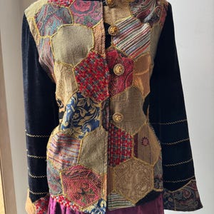 Könnte beinhalten: Eine langärmelige Jacke mit einem Patchwork-Design aus sechseckigen Stoffbahnen in verschiedenen Farben und Texturen, darunter Paisley-, Tweed- und Blumenmuster. Sie hat einen Kragen und Ärmel aus schwarzem Samt, vier goldfarbene Knöpfe und rote Perlen.