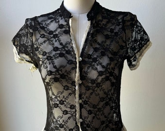 Può includere: Top in pizzo nero con bordino in pizzo bianco e chiusura con bottoni.