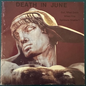 Puede incluir: Una portada de álbum cuadrada con fondo marrón oscuro que presenta una escultura de piedra de una cabeza con casco. El texto DEATH IN JUNE está impreso en la parte superior y el texto But, What Ends When The Symbols Shatter? a la derecha.
