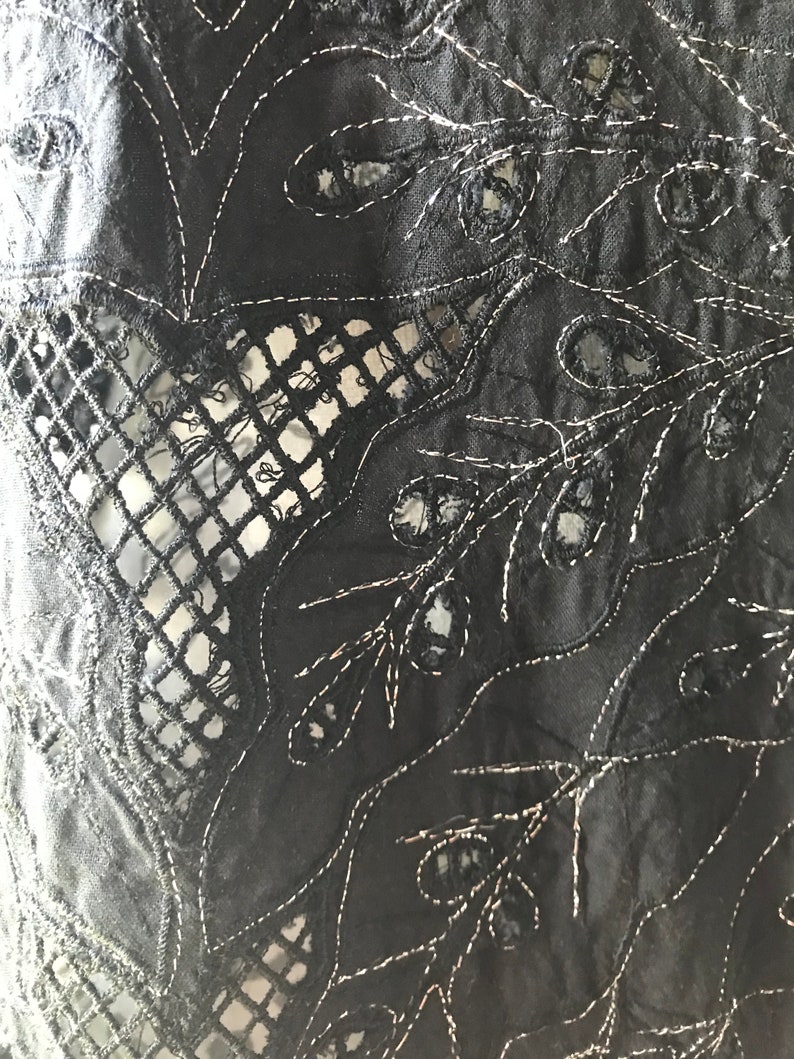 May include: Black fabric with intricate cut-out and embroidered floral designs. The fabric has a delicate, lacy appearance.