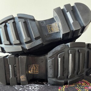 May include: Close-up of the black rubber soles of a pair of shoes. The soles have a textured tread pattern and are designed for grip and traction.
