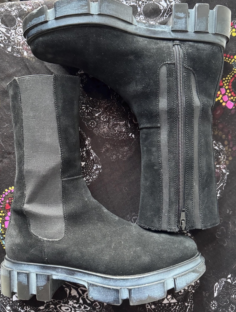 May include: Black suede ankle boots with a chunky rubber sole and a zipper up the back. The boots have a pull-on style and a slightly pointed toe.